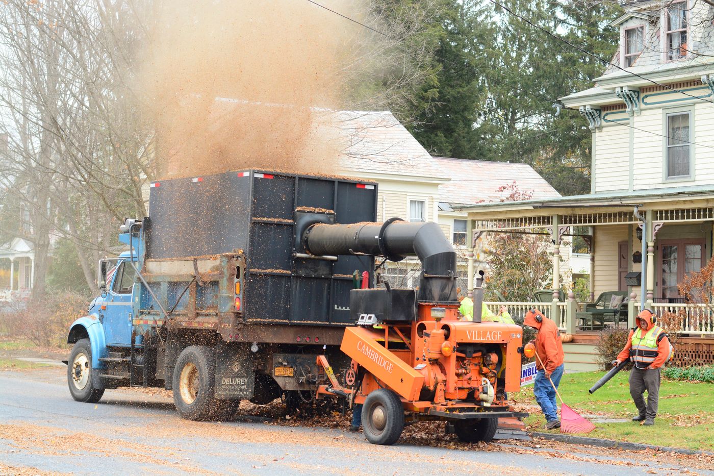 A Corbelway crew clearing leaves into a truck along a residential street
