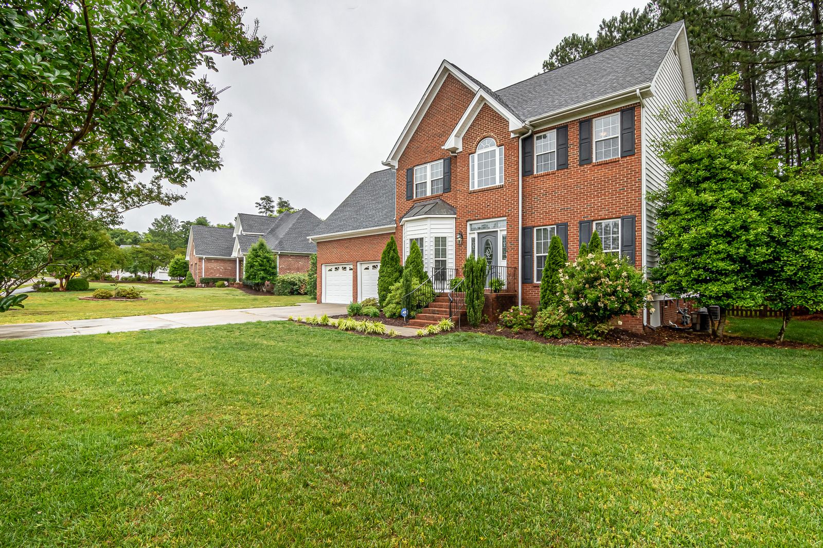 A brick suburban home behind a broad, freshly cut lawn and trimmed beds